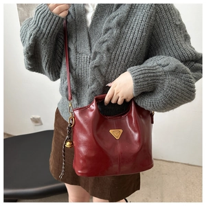 Detail of burgundy glossy leather bucket bag with gold triangle logo and bell charm