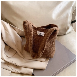 Détail du sac cabas en peluche marron duveteux avec étiquette blanche sur un canapé beige