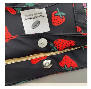 Detail of silver magnetic closure on a black strawberry print tote bag with inner label