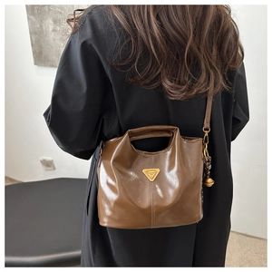 Detail of dark brown glossy leather bucket bag with top handle and metal logo plaque