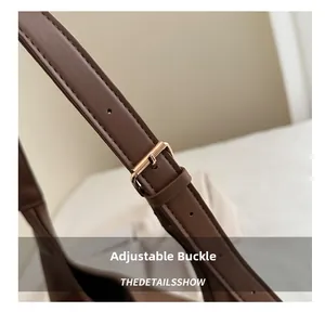 Close-up of the adjustable golden metal buckle on the brown leather shoulder strap