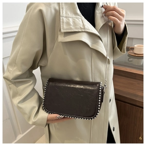 Detail of dark brown glossy leather crossbody bag with silver rivet trim and chain strap