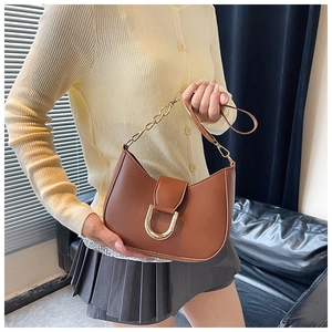 Close-up of brown crescent shoulder bag with large gold U-shaped buckle and chain strap