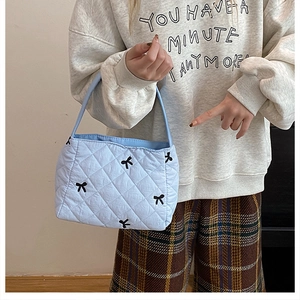 Détail du sac cabas matelassé bleu clair avec motifs de nœuds noirs et texture souple