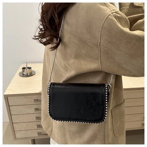 Detail of black leather square bag with silver studs and chain strap on female model