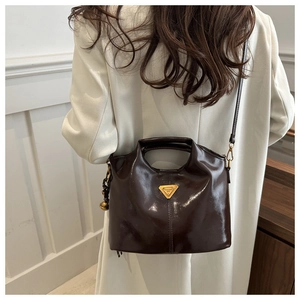 Detail of vintage dark brown glossy leather bucket bag with gold logo and round charm