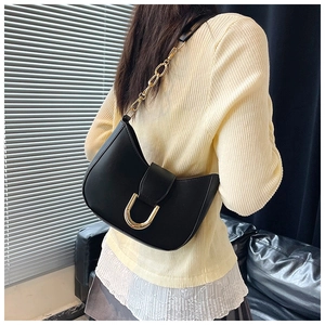 Side view of black crescent shoulder bag with golden U-shaped buckle on dark leather sofa
