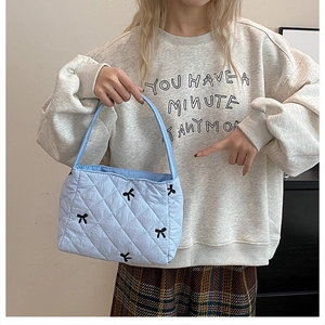 Détail du sac seau matelassé bleu clair avec des nœuds noirs brodés et texture en coton