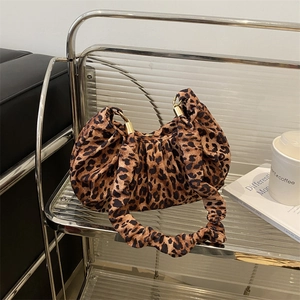 Detail of leopard print pleated shoulder bag with golden metal hardware on a shelf