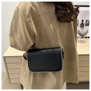 Detailed view of a black crossbody bag with silver rivet edges and chain strap on model