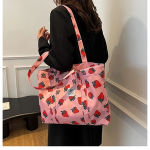 Detail shot of strawberry print pink canvas tote bag worn by model in a minimal setting