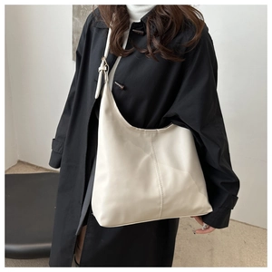 Minimalist cream-colored hobo tote bag with wide strap styled with a black trench coat