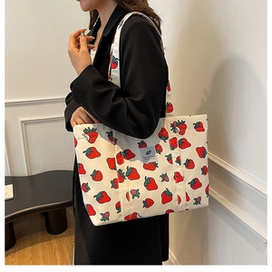 Detail of the strawberry print canvas tote bag carried by a model in a black blazer
