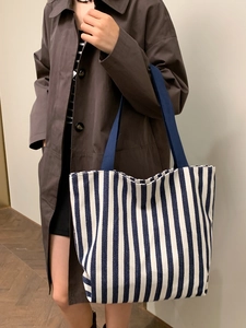 Detailed view of striped canvas tote bag worn by a model in a minimalist indoor setting