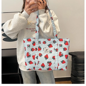 Detail of light blue strawberry print tote bag shown on model in a cozy indoor setting