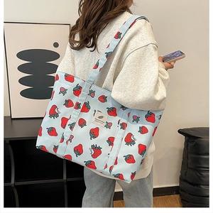 Detailed shoulder view of a light blue canvas tote bag with red strawberry print