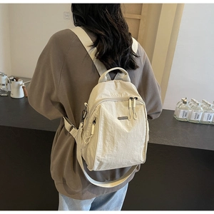 Detail of a cream nylon backpack showing multi-pocket design and fabric shoulder straps