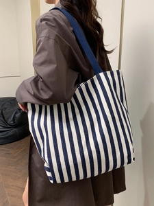Close-up of blue and white striped canvas tote bag worn on shoulder by a model