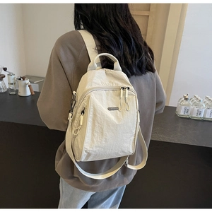 Detail showing beige nylon material with water-repellent texture and zipper pulls on backpack