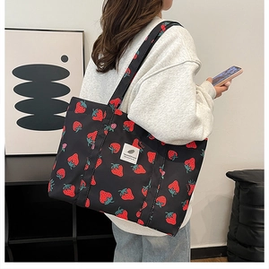 Detailed view of black canvas tote bag with red strawberry pattern and woven label