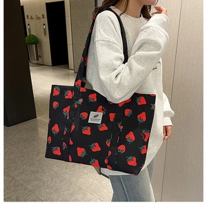 Detail of a black tote bag with red strawberry prints and white woven label on the front