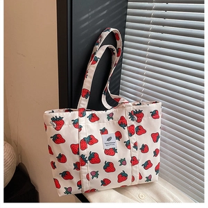 Detail of strawberry print tote bag showing blue logo label and canvas texture