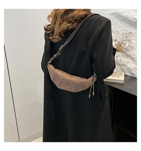 Detailed view of the dark brown suede croissant bag shown on a model's shoulder