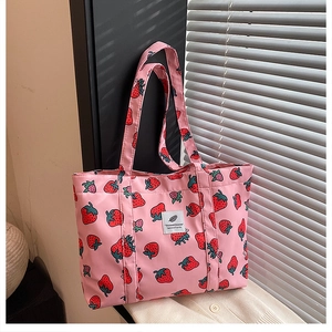 Detail of strawberry print tote bag showing white woven label and soft fabric texture