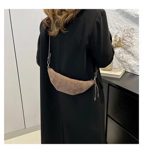 Detail of a dark brown suede crescent shoulder bag with knot strap detail on a female model