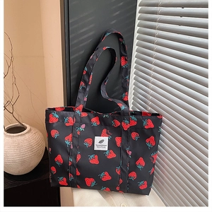 Detailed close-up of strawberry print tote bag with white woven label on black canvas material