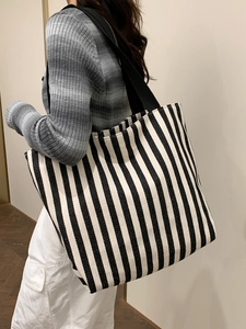Detailed side view of a large capacity striped canvas tote bag worn by a model