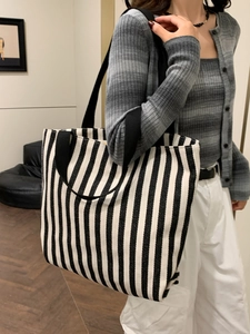 Detail of a large striped canvas tote bag showing its size and wide shoulder straps on a model