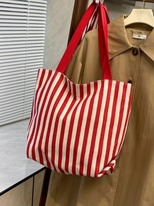 Detailed view of red striped canvas tote bag hanging next to a classic trench coat