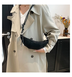 Detail view of black crescent bag with knotted strap and silver hardware on beige trench coat
