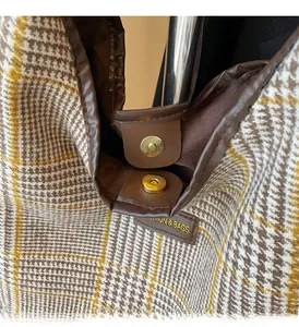 Detail of tweed check tote bag featuring brown faux leather trim and golden magnetic clasp