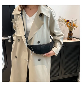 Detailed view of black crescent shoulder bag with pleats on model in beige coat