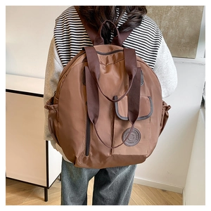 Detail of coffee brown nylon backpack featuring reinforced straps and round logo patch