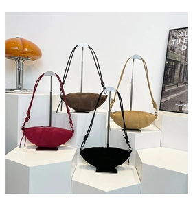 Minimalist croissant shoulder bags in red, brown and black on a minimalist white stand