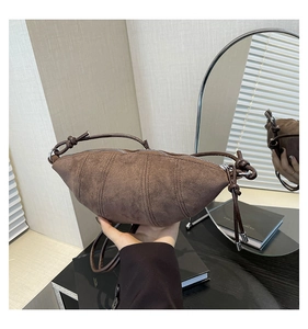 Detail of a brown suede crescent bag with vertical stitching and knotted shoulder strap