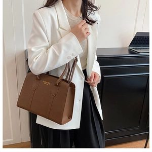 Detail of dark brown faux crocodile tote bag with gold lettering shown on a female model