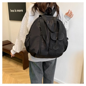 Lifestyle shot of a black minimalist nylon backpack worn by a model in a modern room