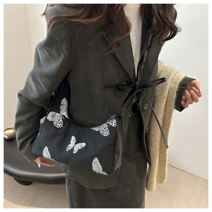 Detail of black underarm bag featuring silver butterfly embroidery and pleated texture