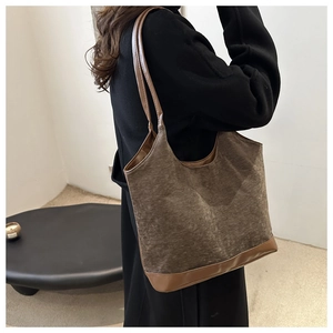 Detail of a brown textured tote bag with leather straps on a model in a black coat