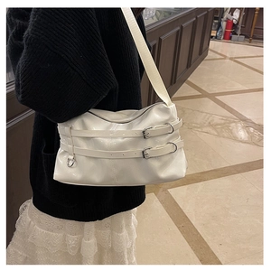 Close-up of white glossy tote bag with decorative leather buckles and wide shoulder strap