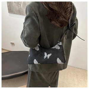 Detail of butterfly embroidery on a black shoulder bag worn over a green blazer