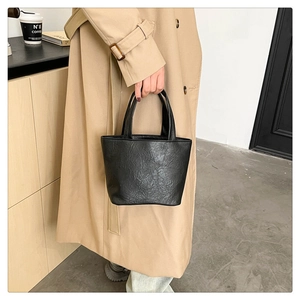 Close-up of black tote bag with soft crinkled texture held by a person in trench coat