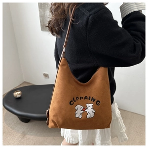 Detail view of brown suede shoulder bag featuring embroidered cute cartoon bears and text