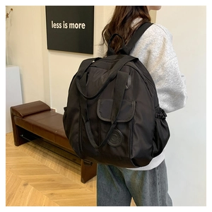 Model wearing a minimalist black nylon backpack with a top handle in a modern studio