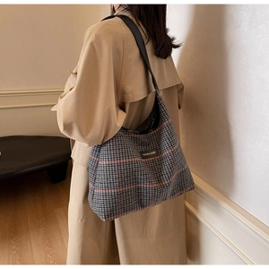 Close-up of a large grey plaid tote bag with thick tweed texture and black logo patch