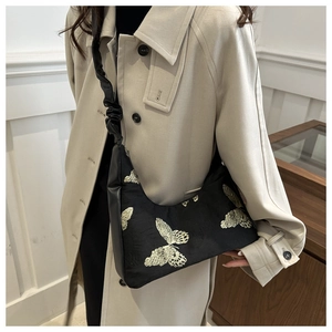 Close-up of golden butterfly embroidery on a black shoulder bag with pleated strap detail